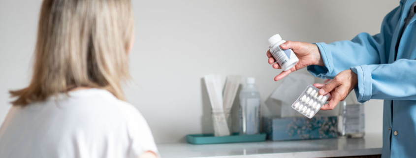 Woman in clinic room looking at a doctor who is holding out two types of probiotic products
