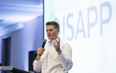 Prof. Kelly Swanson holding a microphone and speaking in front of a screen that shows the ISAPP logo.
