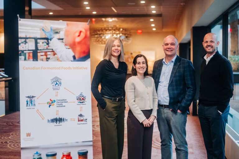 Four people standing in a conference hall in front of a placard about the Canadian Fermented Foods Initiative