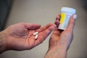 Hand holding probiotic capsules, other hand holding bottle.