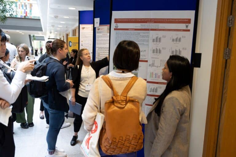scientific posters displayed in an atrium, with people looking and pointing at the posters