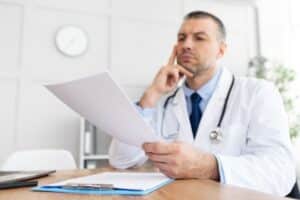 Doctor looking at paper, with hand resting on face in confused manner