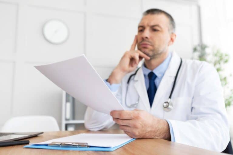 Doctor looking at paper, with hand resting on face in confused manner