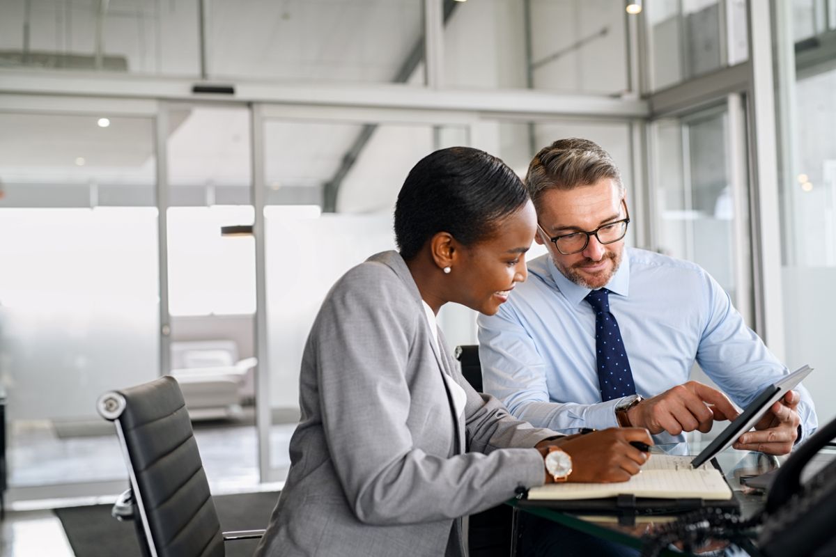 Two business people or scientists sitting together at a table, looking at a phone screen together.